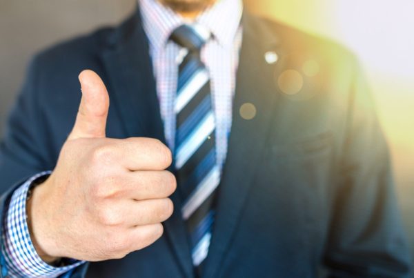 A man in a suit and tie gives a thumbs-up gesture, with the sunlight shining behind him. His face is out of focus, emphasizing his positive gesture—perfect for promoting GoodSuite’s trusted copier services.
