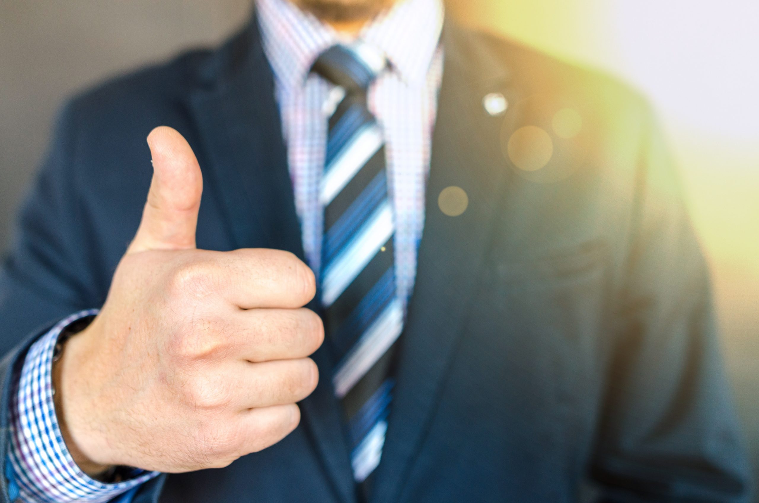 A man in a suit and tie gives a thumbs-up gesture, with the sunlight shining behind him. His face is out of focus, emphasizing his positive gesture—perfect for promoting GoodSuite’s trusted copier services.