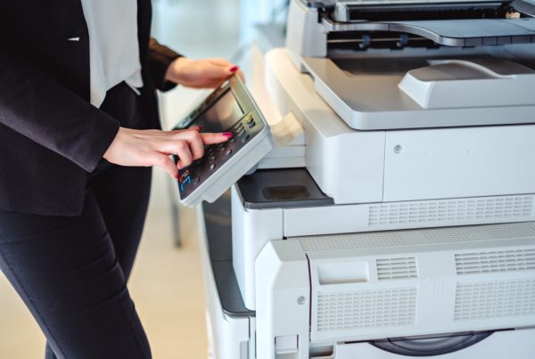 A person in business attire uses the touchscreen control panel of a large office photocopier, preparing to make copies or scan documents—ideal for those considering a copy machine lease in Woodland Hills.