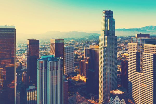 Aerial view of downtown Los Angeles skyscrapers bathed in warm sunlight, with mountains in the background under a clear blue sky—capturing the vibrant energy that inspires top Los Angeles Printing Solutions.