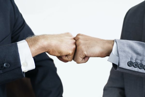 Two people in business suits giving each other a fist bump, symbolizing strategic growth and teamwork, with a plain white background.
