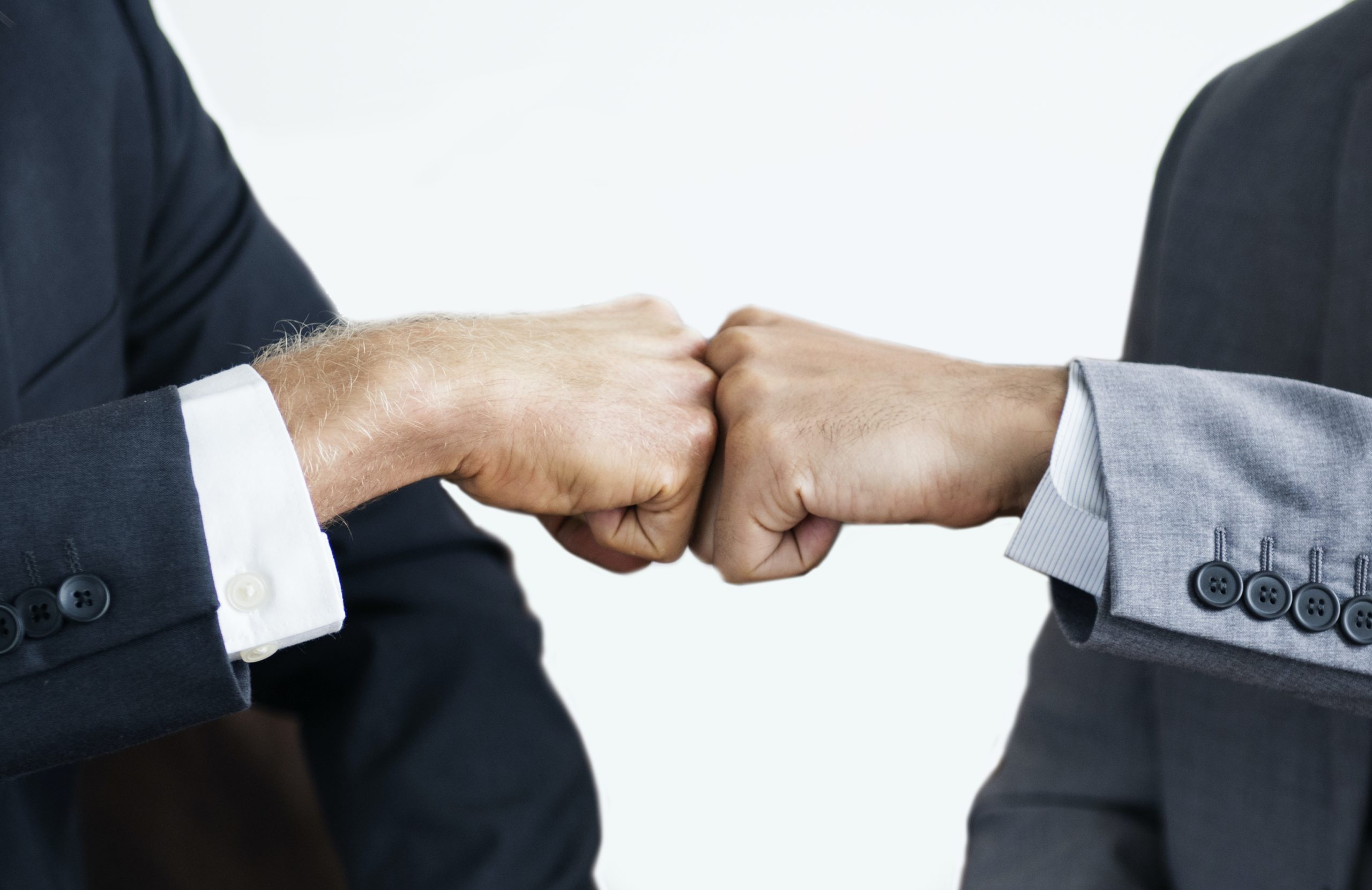 Two people in business suits giving each other a fist bump, symbolizing strategic growth and teamwork, with a plain white background.
