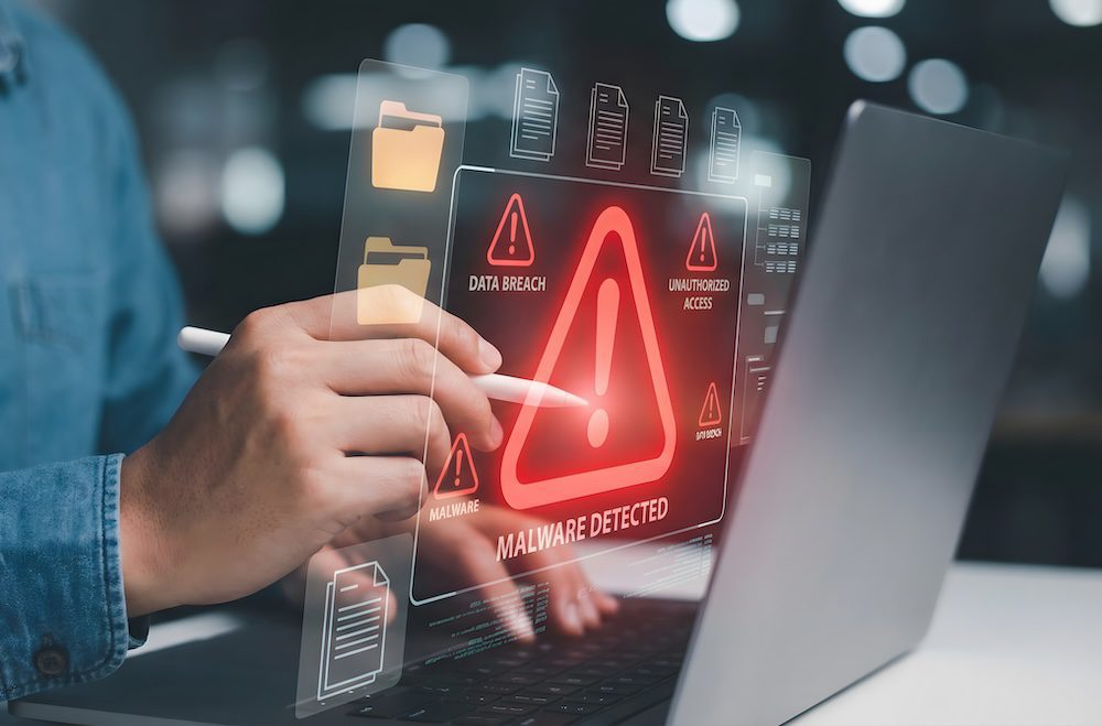 A person using a laptop with a digital display showing a red warning for Malware Detected and alerts for data breach and unauthorized access, highlighting the importance of cyber security against evolving online threats.