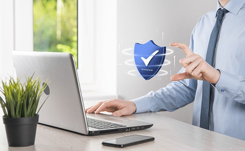 A person in business attire sits at a desk with a laptop, touching a floating digital shield with a check mark, symbolizing essential cybersecurity facts. A potted plant and smartphone are also on the desk.