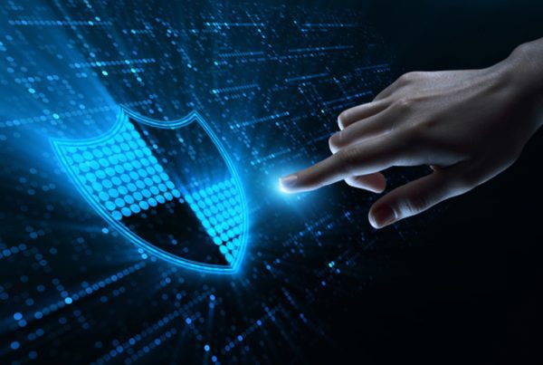 A hand reaching out to touch a glowing digital shield icon, symbolizing cybersecurity or data protection in 2022, with a futuristic blue and black background featuring digital patterns.