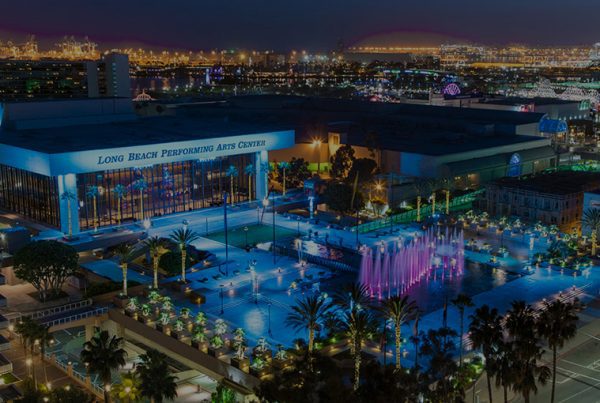 A nighttime view of the Long Beach Performing Arts Center during the CITE Annual Conference, with colorful illuminated fountains, city lights in the background, and conference booths nestled among palm trees and modern buildings.