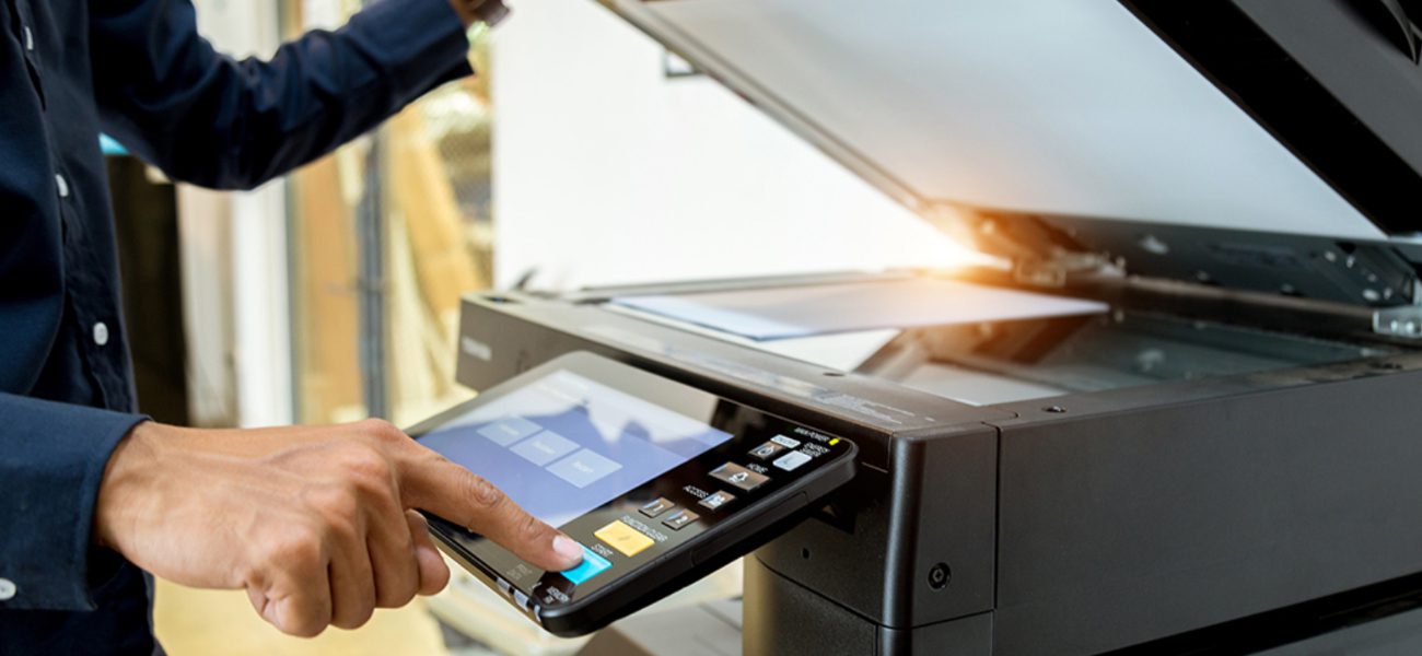 A person using a photocopier, pressing buttons on the control panel while lifting the lid to scan a document—streamlining business tasks with efficient printer services.
