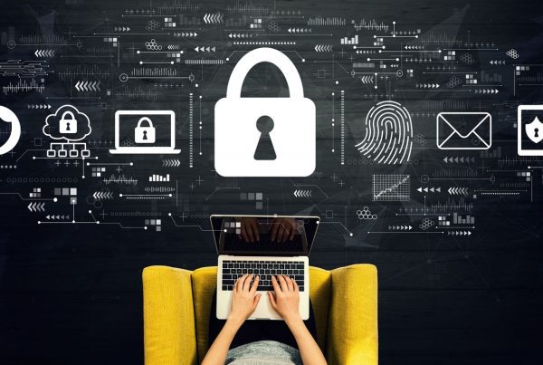 Person typing on a laptop in a yellow chair, with cybersecurity icons like a lock, fingerprint, shield, and envelope above them, representing digital security, data protection, and hybrid work security.