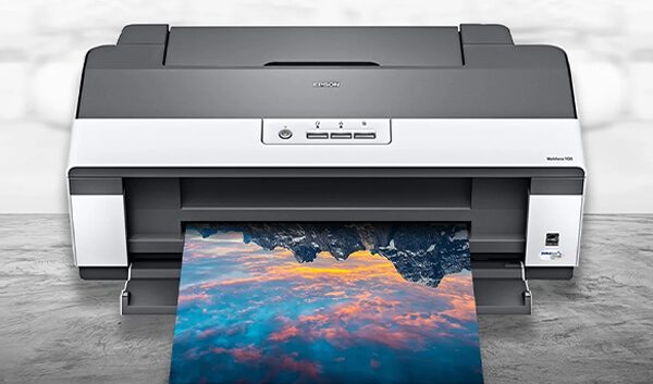 A color printer on a wooden surface is printing a vibrant photo of mountains with a colorful sky reflected in water—showing why it’s important to pick the right printer for stunning results.