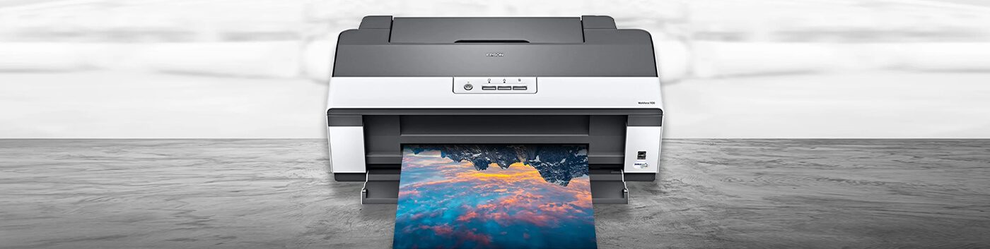 A color printer on a wooden surface is printing a vibrant photo of mountains with a colorful sky reflected in water—showing why it’s important to pick the right printer for stunning results.