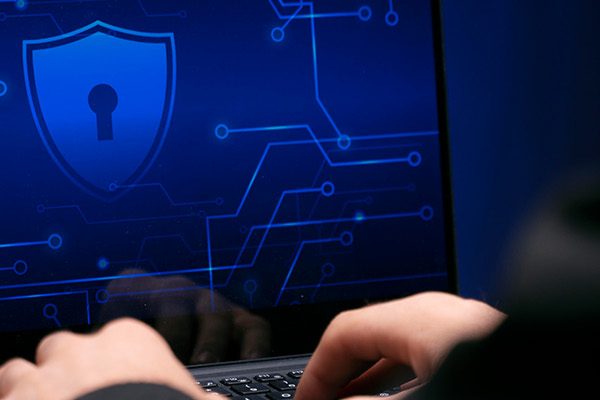 A person types on a laptop displaying a blue digital security interface with a shield and keyhole icon, highlighting business cybersecurity and advanced data protection solutions.