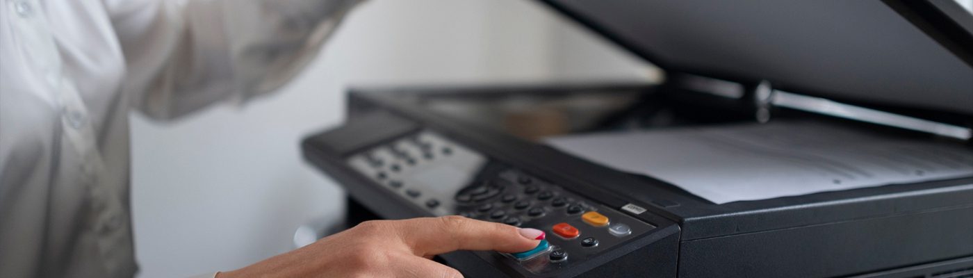 A person presses a button on a photocopier or printer, with papers placed on the scanner bed and the lid open, demonstrating efficient office printing.