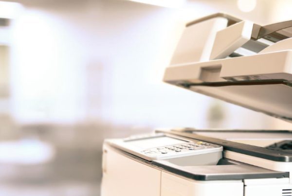 A close-up of a business copier with its lid open in a bright, modern office setting. The background is blurred, emphasizing the best copier’s control panel and scanning bed.
