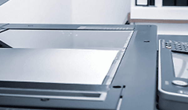 A close-up of a person's hand pressing buttons on a business printer control panel, with the copier lid open in an office setting—ideal for illustrating print maintenance or printer troubleshooting.