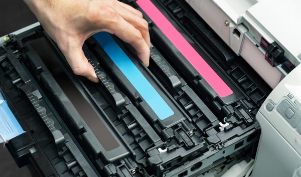 A person’s hands installing or replacing toner cartridges in a color laser printer, demonstrating printer troubleshooting with visible cyan, magenta, and black cartridges.