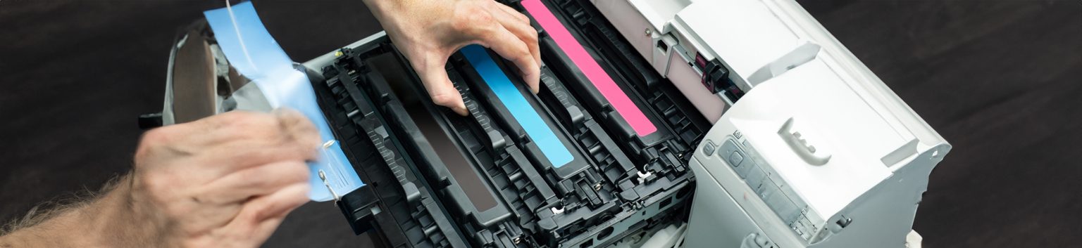 A person’s hands installing or replacing toner cartridges in a color laser printer, demonstrating printer troubleshooting with visible cyan, magenta, and black cartridges.