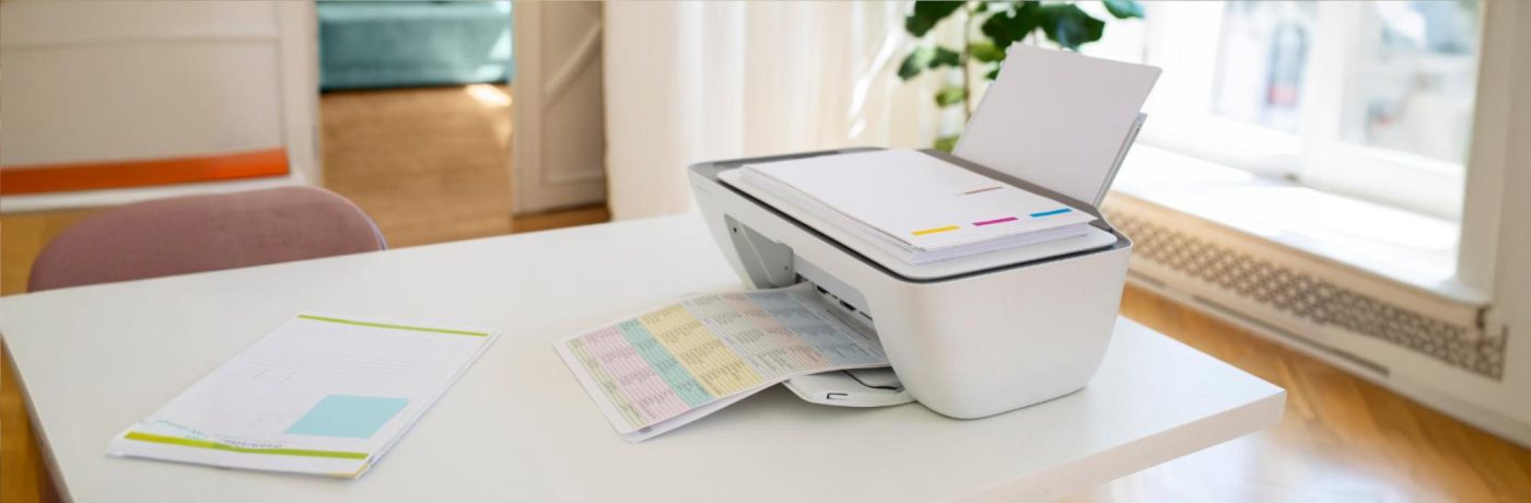 A white printer on a table prints a colorful, chart-filled document—ideal for showcasing benefits in the automotive business. Nearby, a paper with charts and text lies flat. The bright room features home office decor and ample natural light.