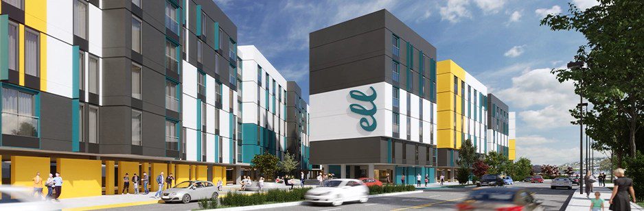 A modern, colorful apartment complex with gray, white, yellow, and teal panels, much like GoodSuite’s innovative approach to vendor consolidation. People stroll the sidewalk and cars are parked along the road under a blue sky with scattered clouds.