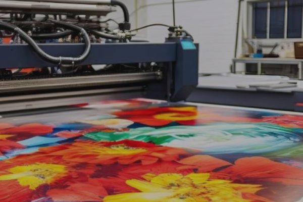 A large industrial printer creates a vibrant, colorful print featuring red, yellow, and orange flowers in a modern commercial printing shop, with shelves and equipment visible in the background—perfect for impactful print marketing.