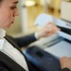 A woman in business attire lifts the lid of a photocopier in an office, preparing to scan a document—highlighting how law firms can reduce printing costs with effective managed print services.