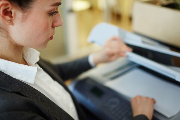 A woman in business attire lifts the lid of a photocopier in an office, preparing to scan a document—highlighting how law firms can reduce printing costs with effective managed print services.