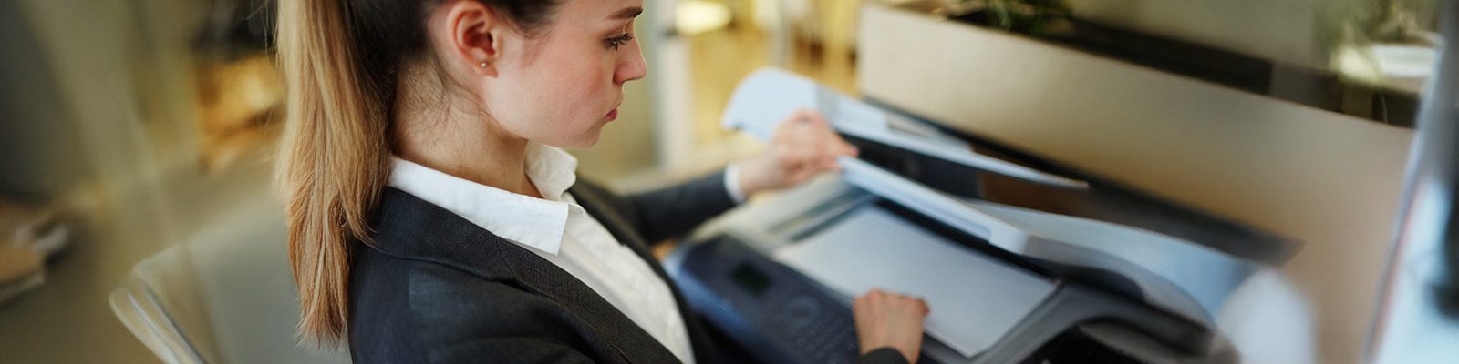 A woman in business attire lifts the lid of a photocopier in an office, preparing to scan a document—highlighting how law firms can reduce printing costs with effective managed print services.