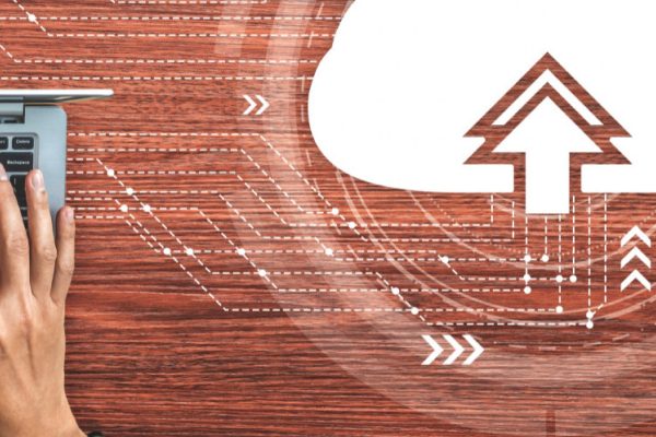 Hands typing on a laptop keyboard on a wooden desk, with digital cloud upload icon and technology symbols overlaid, representing the future of cloud computing for small businesses and efficient data transfer.