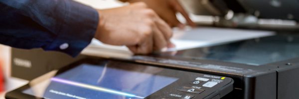 A person places a sheet of paper on the glass of a photocopy machine, demonstrating print management essentials for small businesses in an office setting.