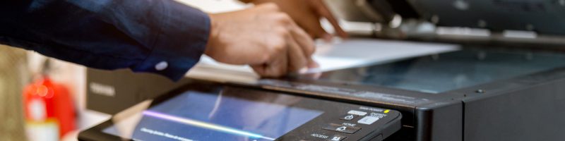A person places a sheet of paper on the glass of a photocopy machine, demonstrating print management essentials for small businesses in an office setting.