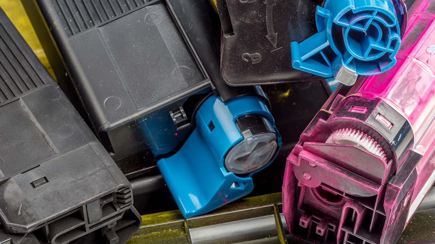 Close-up of several used printer toner cartridges in black, cyan, and magenta colors, stacked together with visible gears and plastic components—perfect for promoting printer cartridge recycling initiatives.