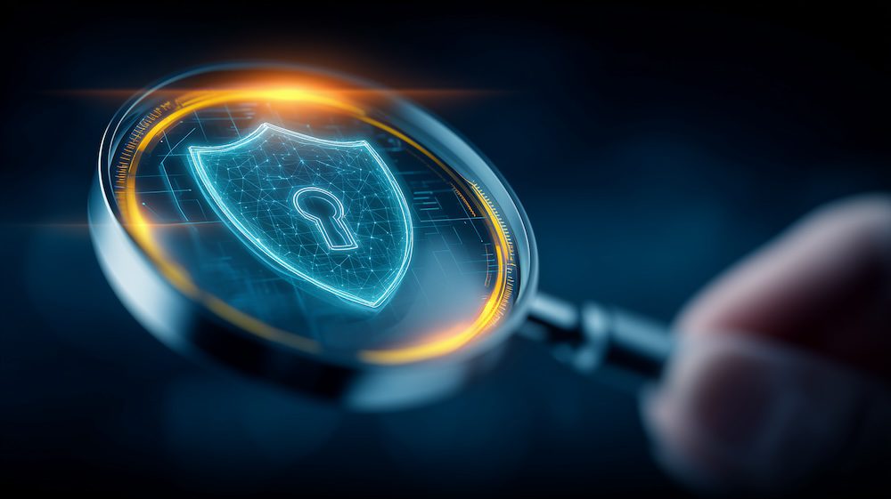 A hand holds a magnifying glass focused on a glowing digital shield with a keyhole, symbolizing CCPA compliant cybersecurity or data protection, against a dark, blurred background.