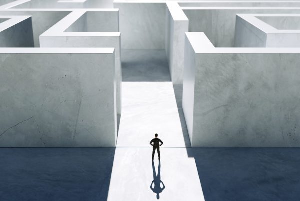 A person stands at the entrance of a large, white maze, casting a long shadow on the ground, appearing to contemplate which path to take—a minimalistic scene capturing the confusion often faced by growing businesses.