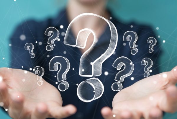 A person holds their open hands forward, with multiple white, hand-drawn question marks floating above their palms—symbolizing how an IT team tackles both big ones and small problems against a blurred blue background.