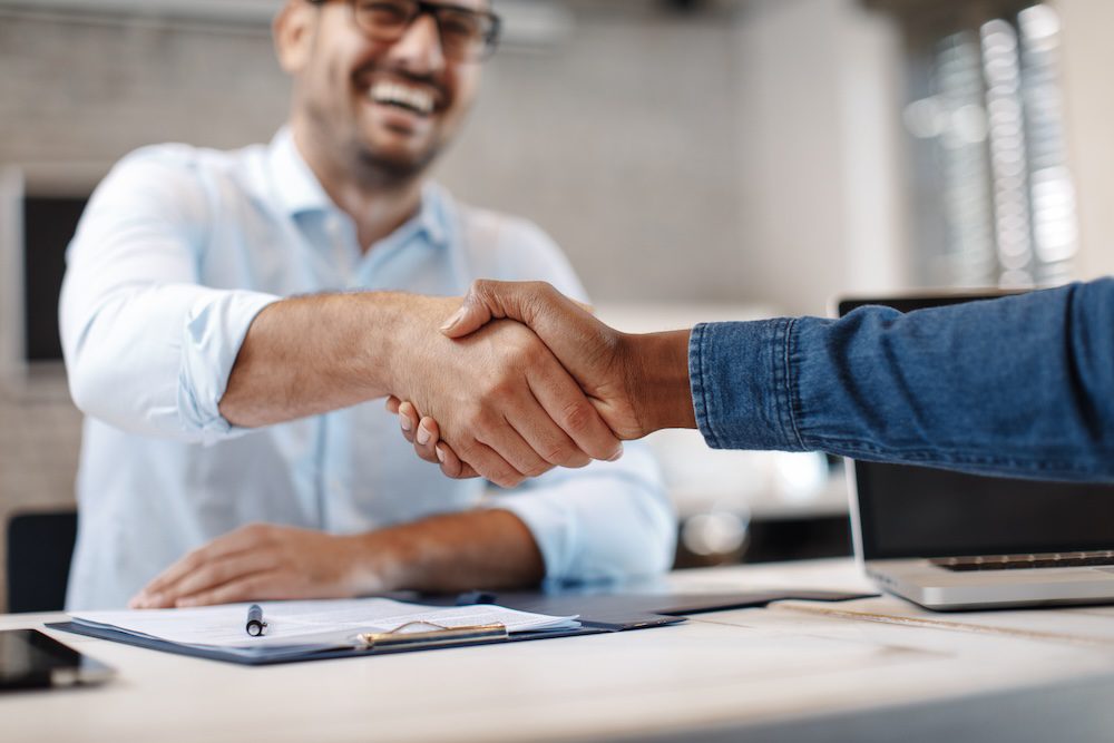Two people shaking hands across a desk in an office setting. concept of customer trust and cybersecurity.