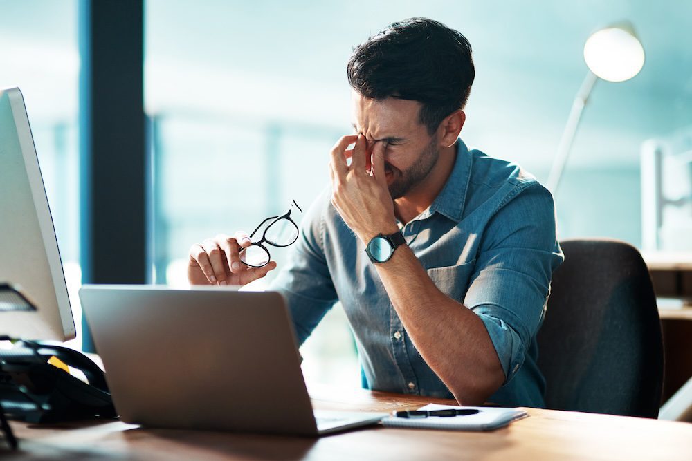 a man frustrated at his computer. a cybersecurity breach has stopped his work.