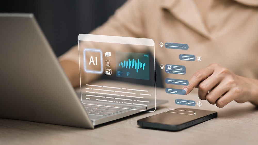 A person interacts with virtual AI interface graphics projected above a laptop and smartphone, suggesting AI technology and digital communication in a modern workspace—alluding to the seamless integration of shadow AI within everyday workflows.