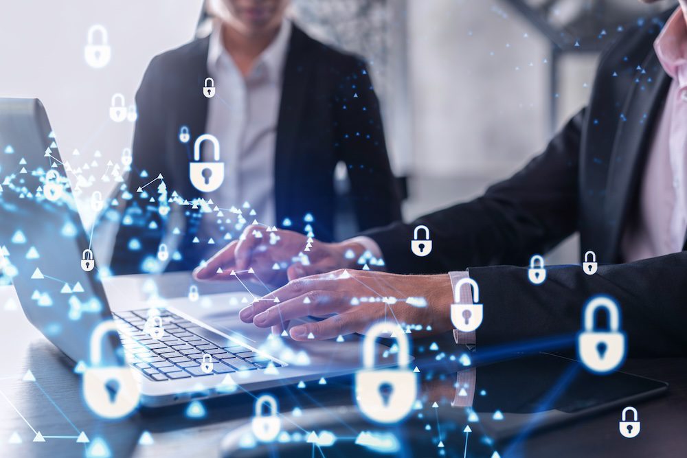 Two people in business attire work on laptops, with digital lock icons overlaid, symbolizing cybersecurity and data protection. The scene highlights the importance of following cybersecurity best practices for small businesses in today’s digital landscape.